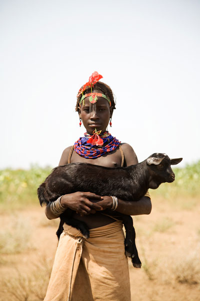 Girl Holding Goat with Baobab flower through lip, Omo Valley, Ethiopia. © Andrew Geiger